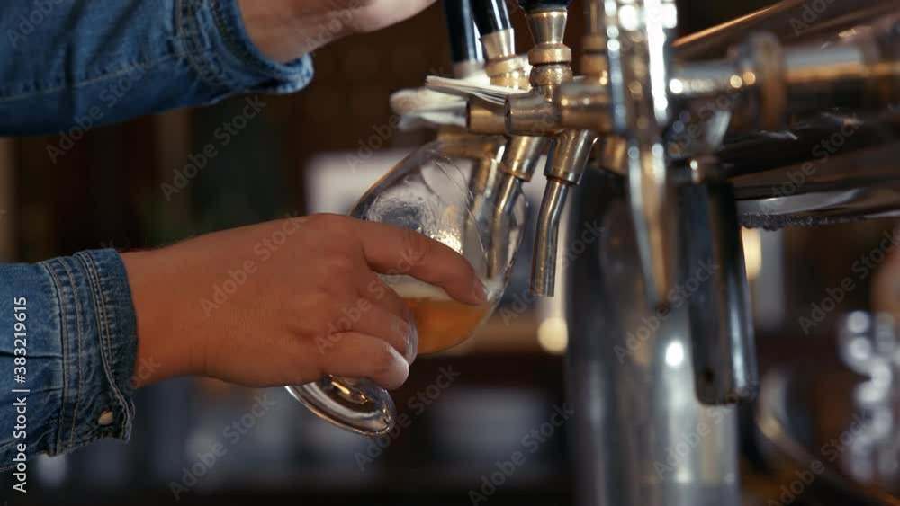 Close up of barkeepers hands draft glass of beer with foam crown shot in 4k super slow motion