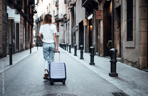 Young traveling woman with suitcase on a sunny city street. Traveler on vacation. photo