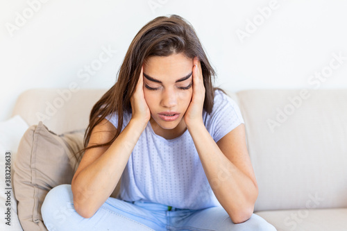 Sad and depressed young woman sitting on a couch in the living room at home