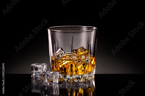 Crystal glass of whiskey with ice cubes on black background.