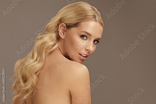 Beautiful adult girl with wavy blond hair on beige isolated background. Female beauty portrait  copy space close-up.