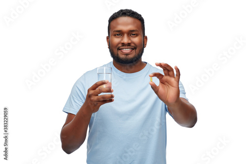 medicine, health and people concept - happy smiling african american man with pill and glass of water over white background