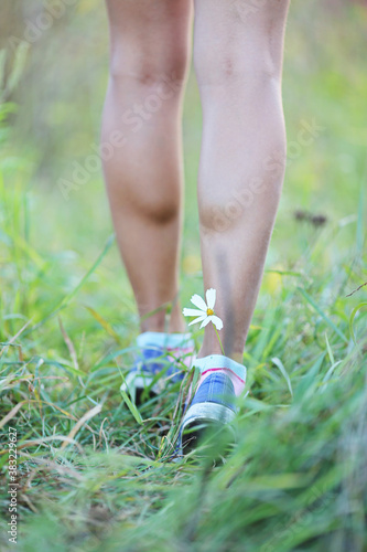 young fitness woman legs walking at forest grass. Flower in shoes. Sport and nealthy lifestyle concept