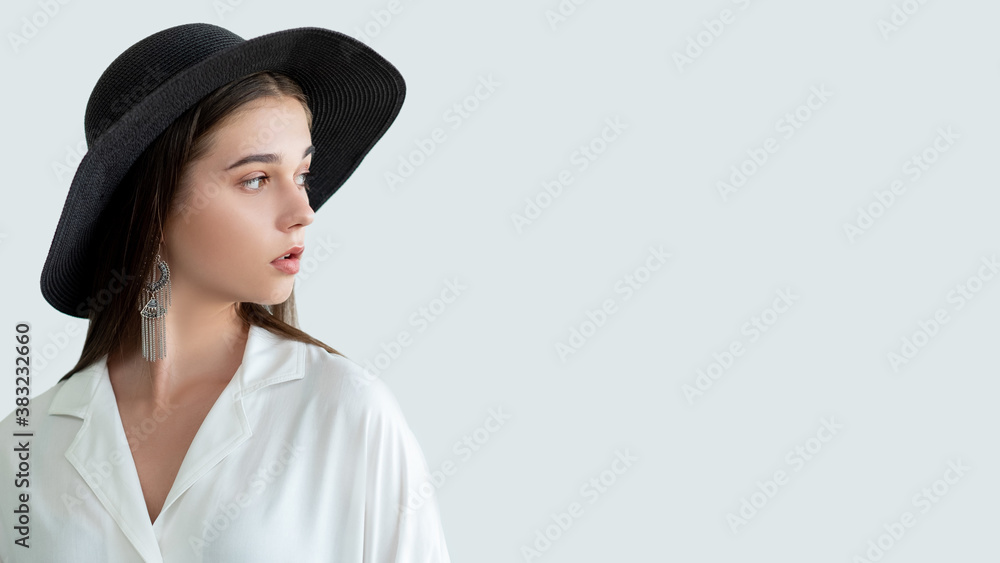 Fashion look. Trend summer outfit. Beautiful woman in straw black hat vintage earrings white blouse isolated on neutral copy space. Female elegance. Casual style. Advertising background Fashion look. Trend summer outfit. Beautiful woman in straw black hat vintage earrings white blouse isolated on neutral copy space. Female elegance. Casual style. Advertising background