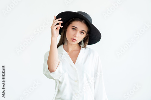 Trend fashion look. Casual style shooting. Elegant young woman in wide-brimmed black hat vintage earrings white shirt isolated on neutral. Boho lifestyle. Advertising background