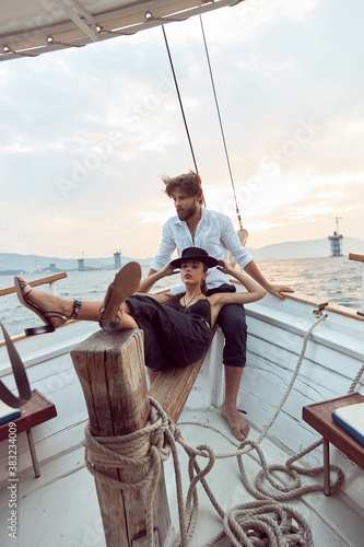 a romantic trip by sea on the yacht of a stylish couple in love, who emotionally show their feelings.he is wearing a white linen shirt and pants, she is wearing a black top, pants and a hat © monchak
