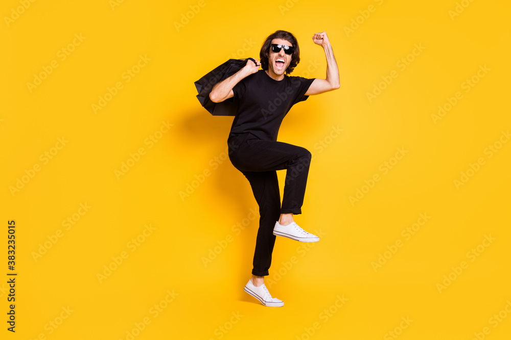 Full length photo of young man hold shopping packages open mouth wear black t-shirt pants white sneakers sunglass isolated yellow color background