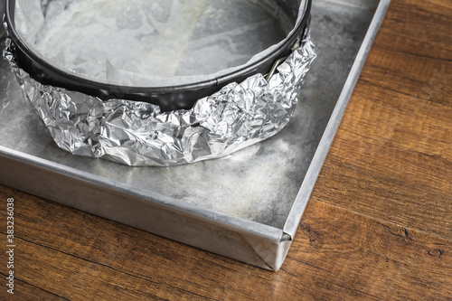 A cake tin line with wax paper and wrap in aluminum foil on a tray for putting a water bath before baking a cheesecake in the oven.