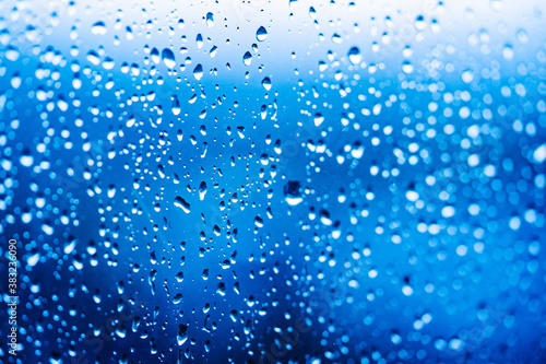 Droplets of water on enlighted glass background. Rain water drops running down. Water droplets falling on glass surface.