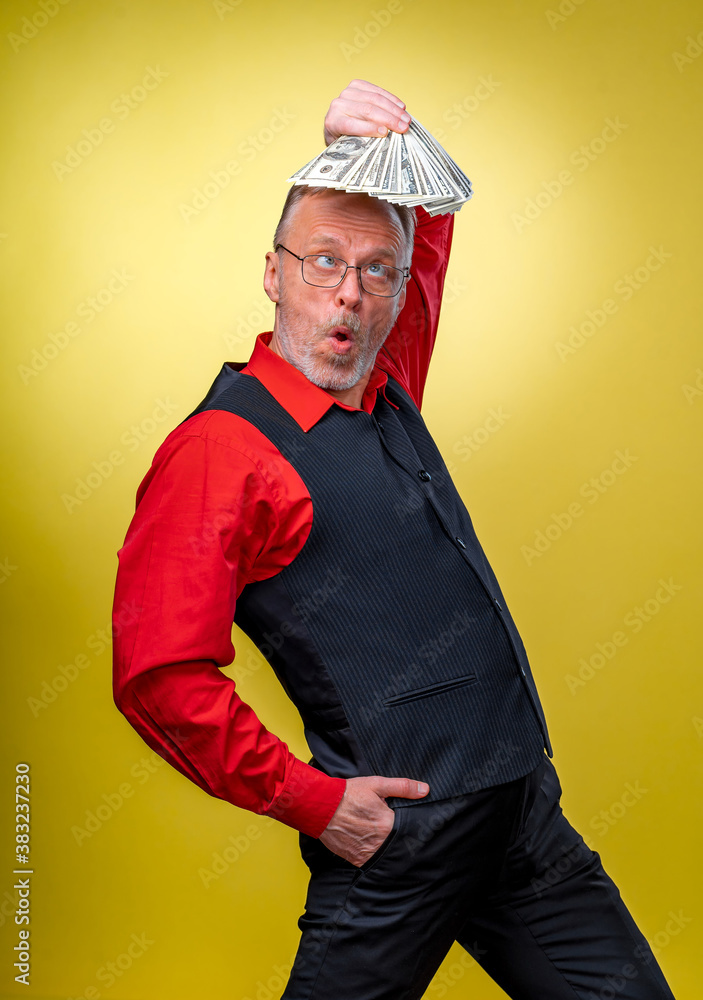 Old smiling grey-haired man in eyeglasses holding fan of dollars over head in dancing pose. Human emotions and facial expressions. Old smiling grey-haired man in eyeglasses holding fan of dollars over head in dancing pose. Human emotions and facial expressions.