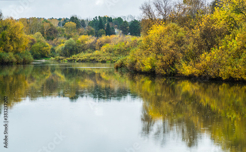 Calm river with trees on the shores in rainy autumn day. Autumn landscape. 