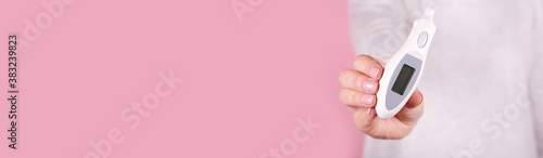 Electronic thermometer in hands on a pink background. Close up photo, copy space template, banner.