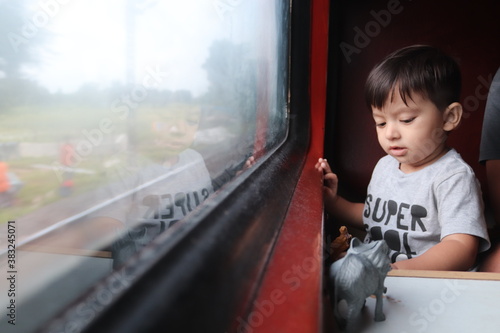small cute indian baby boy sitting at train window seat and playing with toys