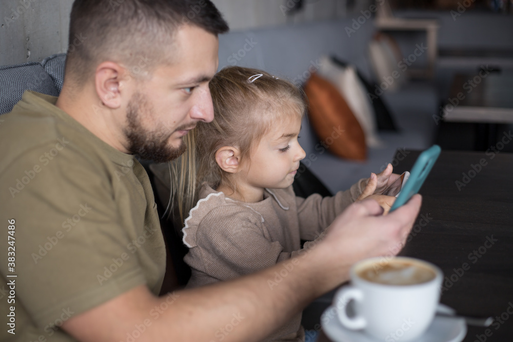 Father with little girl spend time in cafe, addicted to theirs smartphones. Man and child playing playing with phone in cafe. Father with little girl spend time in cafe, addicted to theirs smartphones. Man and child playing playing with phone in cafe.