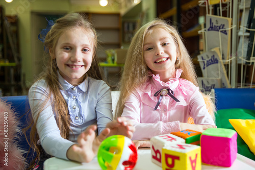 Two funny girls playing with alphabet blocks in the library