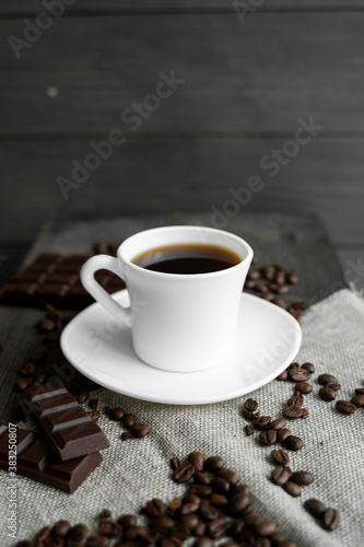Coffee cup with cookies and chocolate with scattered coffee beans on linen and wooden table background. Mug of black coffee.