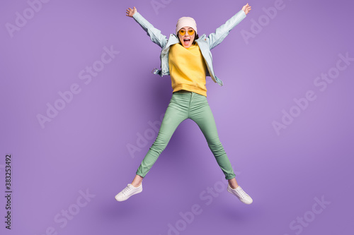 Full body photo of funky pretty lady stylish clothes jump high rejoicing spread hands star shape wear sun specs casual hat modern jacket green pants footwear isolated purple color background © deagreez