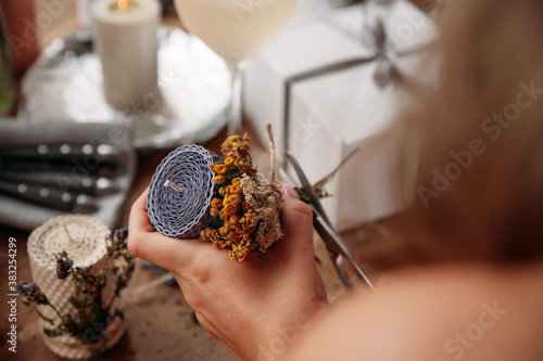 DIY wax candle making process. Woman making decorative wax candle and decorates with dried flowers, close-up of hands