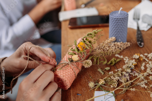 DIY wax candle making process. Woman making decorative wax candle and decorates with dried flowers, close-up of hands