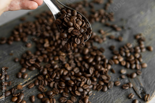 Fresh roasted arabica coffee beans in a metal spoon and scattered coffee beans on a wooden table.