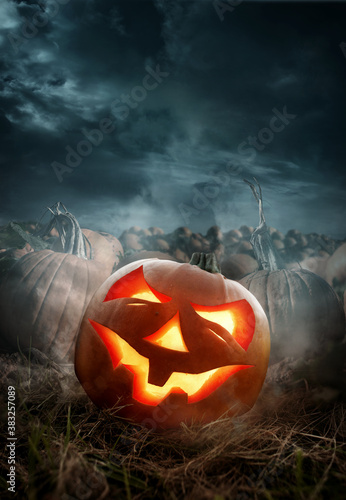 Halloween pumpkin field with a glowing carved pumpkin Jack O lantern at night. Photo composite.