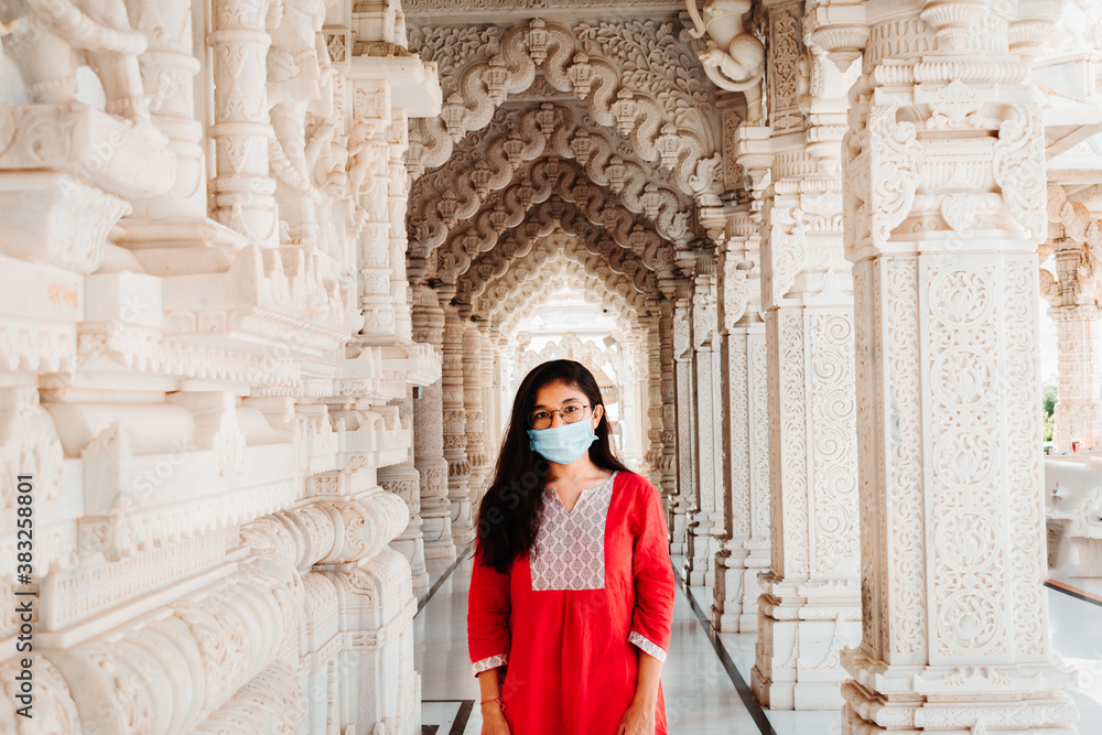 Portrait of Indian female model in mask standing at temple and staring at camera. Concept of wearing mask at public places
