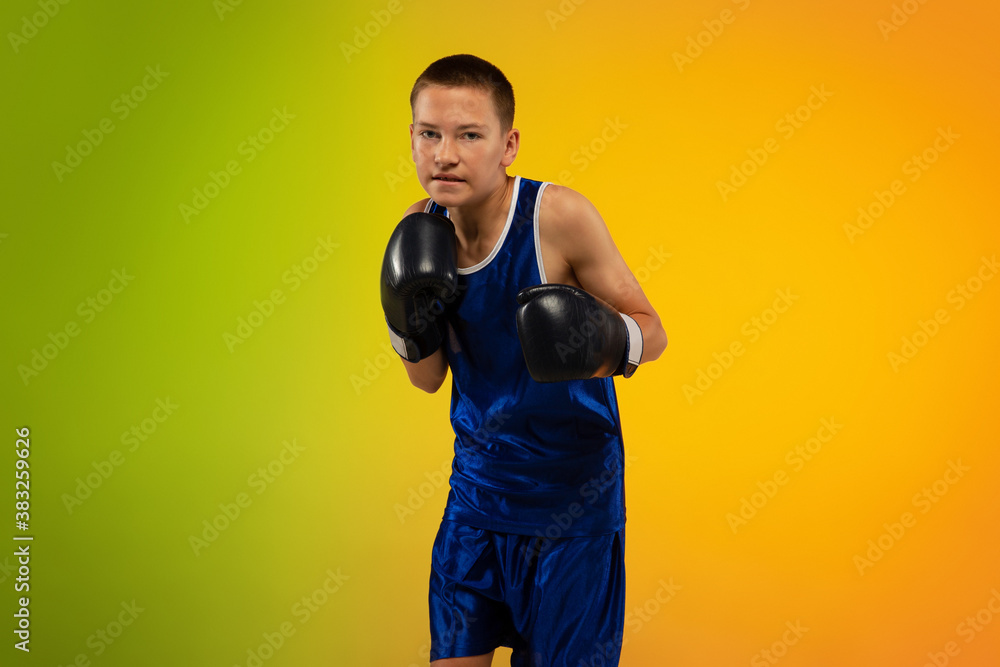 Angry. Teenage professional boxer training in action, motion isolated on gradient background in neon light. Kicking, boxing. Concept of sport, movement, energy and dynamic, healthy lifestyle.