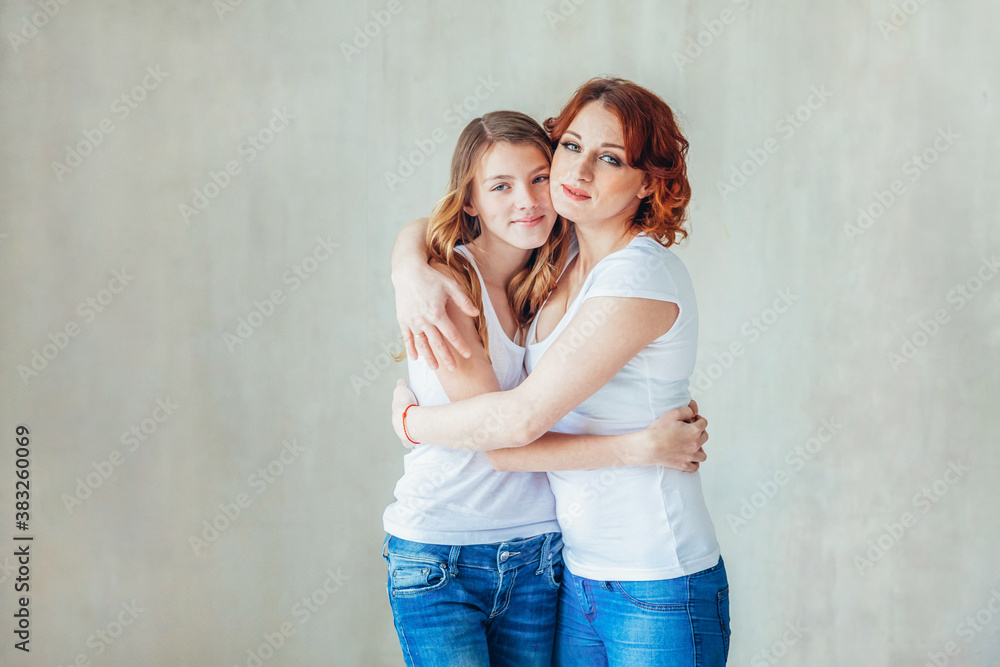 Young mother embracing her child. Woman and teenage girl relaxing in white bedroom near gray wall indoors. Happy family at home. Young mom playing with her daughter