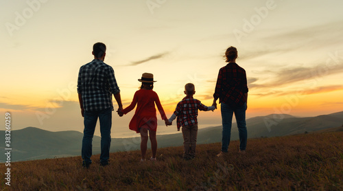 Happy family: mother, father, children son and daughter stand with their backs holding hands on sunset.