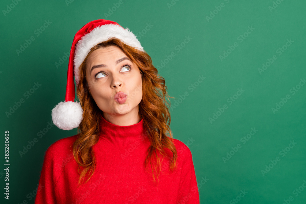 Photo of funny charming lady look up empty space pout lips wear red pullover x-mas cap isolated green color background Photo of funny charming lady look up empty space pout lips wear red pullover x-mas cap isolated green color background
