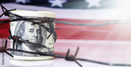 Sanctions and embargo busting. Close up US Dollar bills and barbed wire as symbol of economic warfare. Horizontal image.