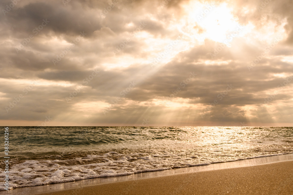 Beautiful sunset on the seashore. The sun's rays shine through the clouds. Focusing on the water's edge.