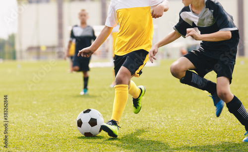 Child kicking soccer ball in a duel. Running footballers compete for the ball. Children attending school soccer tournament game