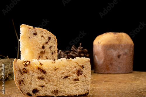 Arrangement with panettone and panettone slices, pine cones on rustic wood, black background, selective focus.
