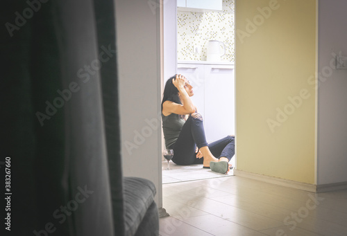 View to kitchen with young beautiful caucasian woman  on the kitchen floor looking  up to the light with hand on her forehead and glass of wine on the ground photo