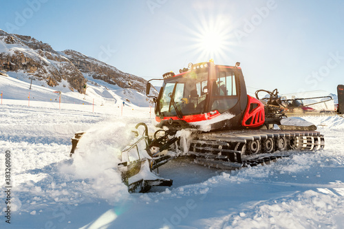 Red modern snowcat ratrack with snowplow snow grooming machine preparing ski slope piste hill at alpine skiing winter resort Ischgl in Austria. Heavy machinery mountain equipment track vehicle