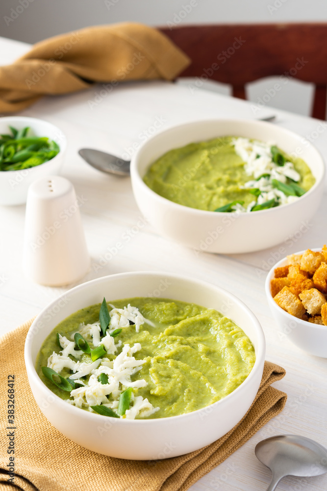Healthy delicious broccoli and cucumber cream puree soup with mozzarella, green onions and croutons, bowl of soup on a white table Healthy delicious broccoli and cucumber cream puree soup with mozzarella, green onions and croutons, bowl of soup on a white table