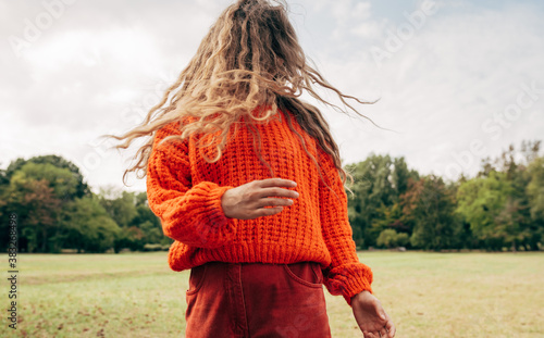 Canvas-taulu Horizontal image of an young woman with blowing long blonde hair wearing an orange sweater posing on the sky and nature background