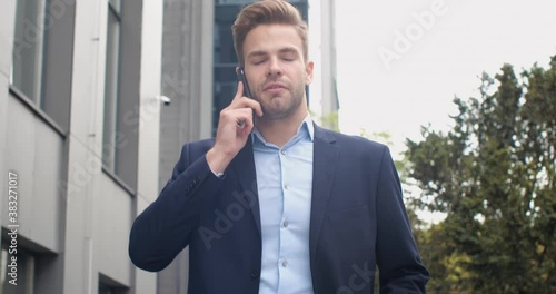 Serious Businessman is talking on his Phone while walking in Business District. Successful Caucasian Male Boss Leader working outdoor, having Busy Lifestyle. Wearing stylish Formal Outfit.Busy People. photo