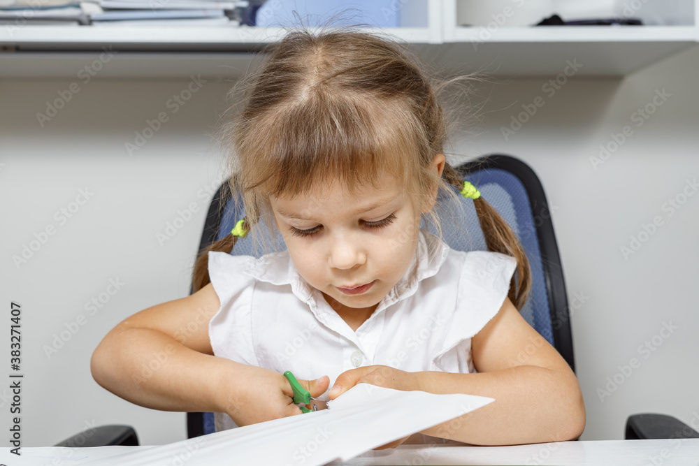 beautiful little girl in a white blouse cuts out of paper. children's creativity beautiful little girl in a white blouse cuts out of paper. children's creativity