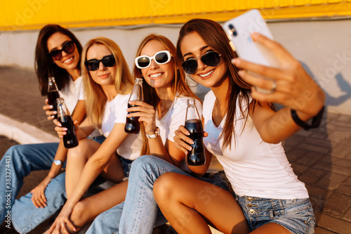 Young friends drinking a drink having fun together and taking a selfie on a mobile phone  against the background of a yellow wall  concept of friendship and celebration