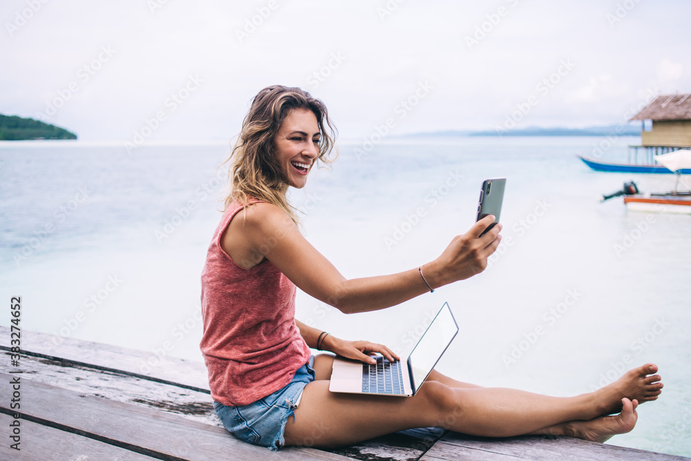 Happy pretty woman taking selfie on pier near ocean
