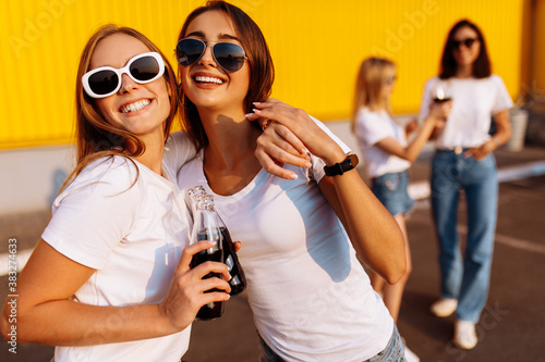 Happy young friends, stylish young women cheerfully walk and drink drinks, summer sunny day, near shopping mall, friendship concept