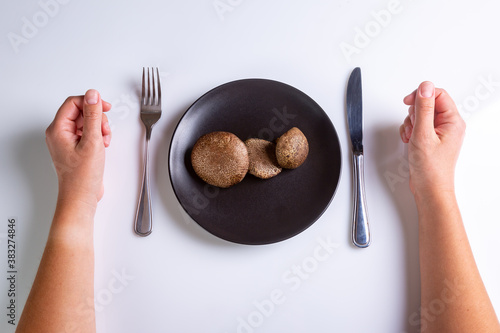 Raw Jersey cow mushroom in a black plate and a knife and fork nearby on a white background top view. Human hands near cutlery. Horizontal orientation. High quality photo photo