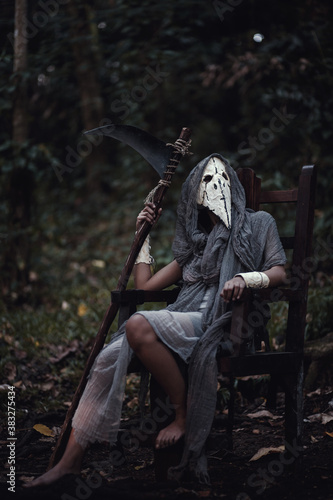 grim reaper holding scythe sitting in the dark forest. Halloween background