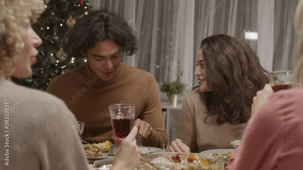 Back view of few multiethnic young women and man sitting at dining table, enjoying food and talking Back view of few multiethnic young women and man sitting at dining table, enjoying food and talking