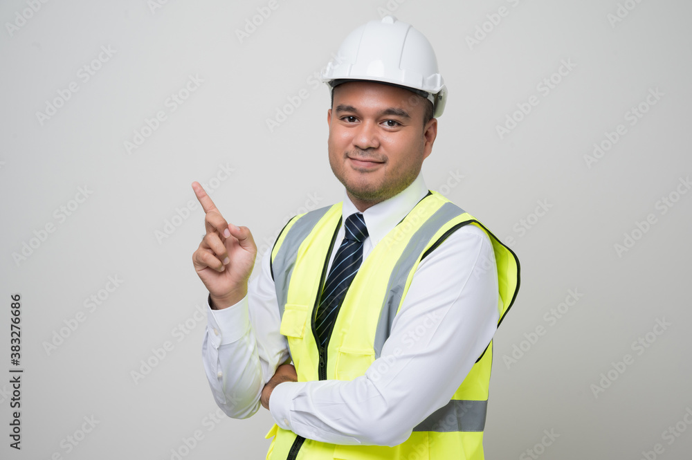Asian worker in uniform hard hat pointing the finger to blank space for advertise text or mockup in studio isolated white background. Asian worker in uniform hard hat pointing the finger to blank space for advertise text or mockup in studio isolated white background.