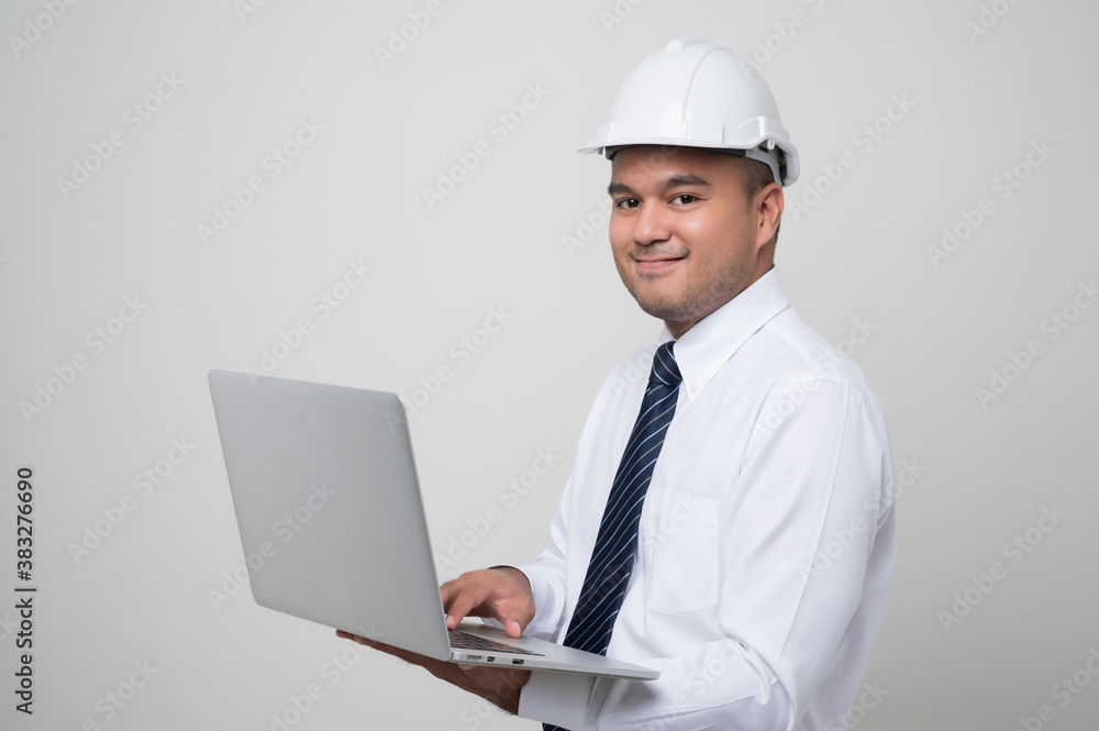 Asian civil engineer operate with laptop to control working in studio. Worker wearing hard hat using laptop computer standing on isolated white background.. Asian civil engineer operate with laptop to control working in studio. Worker wearing hard hat using laptop computer standing on isolated white background..