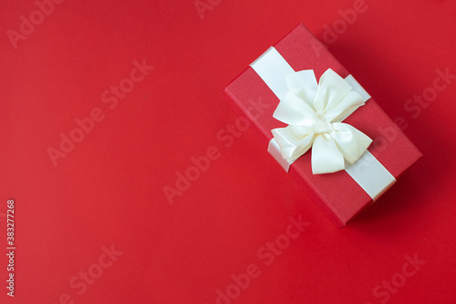 Red gift with white bow on red background. Close up. Top view. Focus on bow