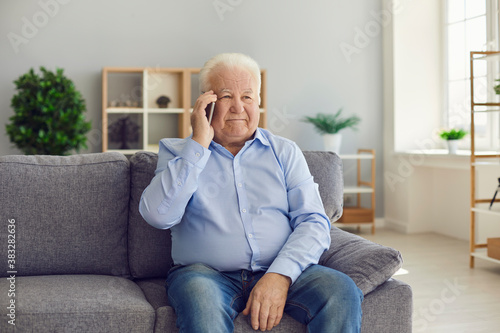 Senior man sitting on couch and making phone call on smartphone to keep in touch with his relatives